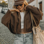 Woman wearing a brown jacket, white top, and jeans on a street.
