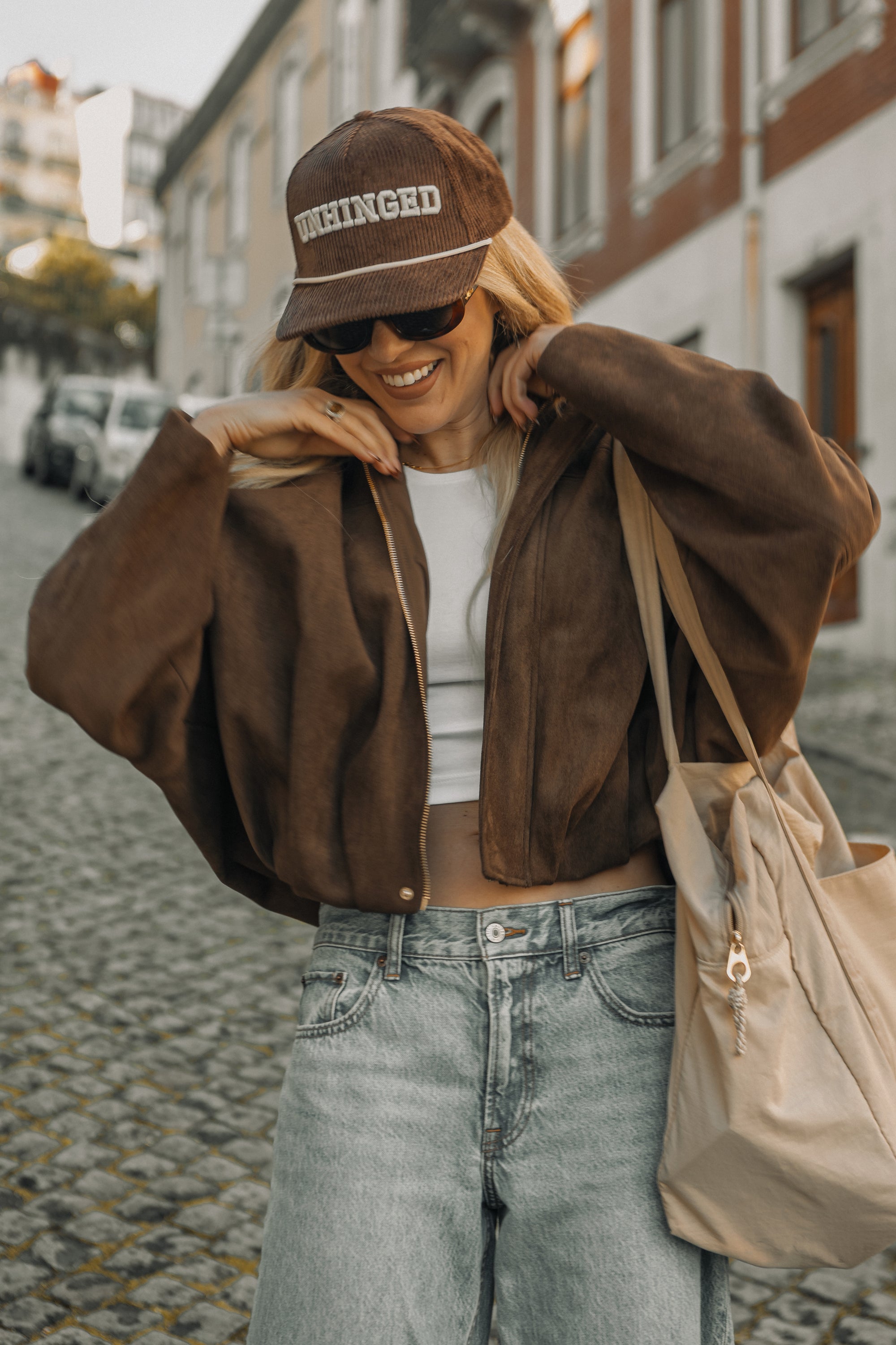 Woman wearing a brown jacket, white top, and jeans on a street.